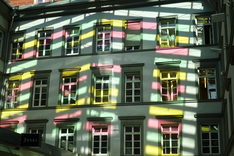 eine Häuserfront mit vielen Farbstreifen, wegen eines Glasdaches und Sonnenschein
